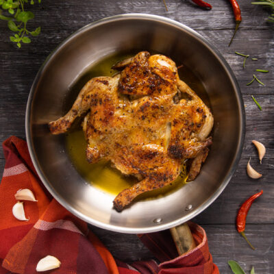 Pollo alla diavola intero appiattito in padella, dorato e speziato con fondo di cottura