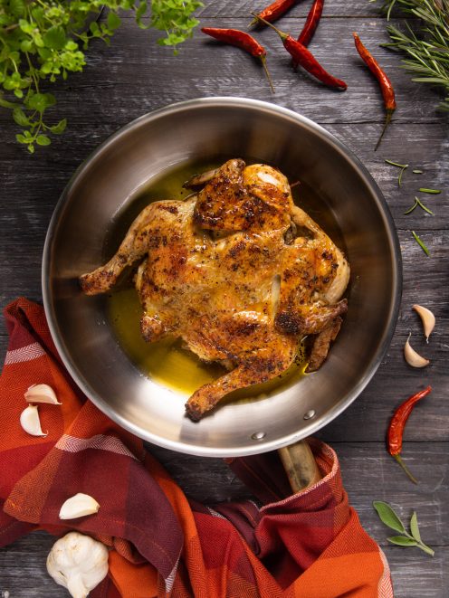 Pollo alla diavola intero appiattito in padella, dorato e speziato con fondo di cottura