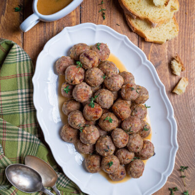 Polpette al forno dorate servite su vassoio con fondo di cottura e rametti di timo