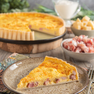 Quiche Lorraine con una fetta servita, ripieno dorato con pezzi di pancetta affumicata