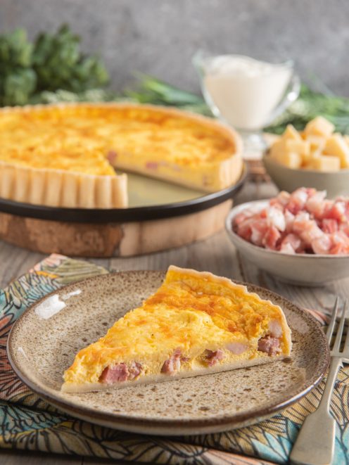 Quiche Lorraine con una fetta servita, ripieno dorato con pezzi di pancetta affumicata