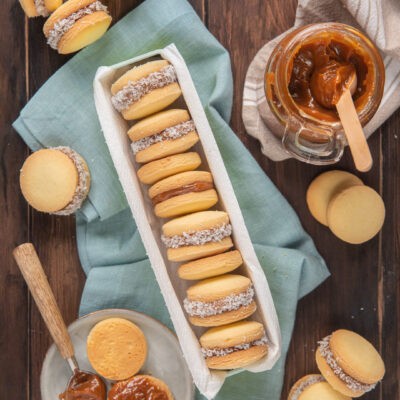Alfajores farciti di dulce de leche e bordati di cocco disposti in fila accanto al vasetto di crema