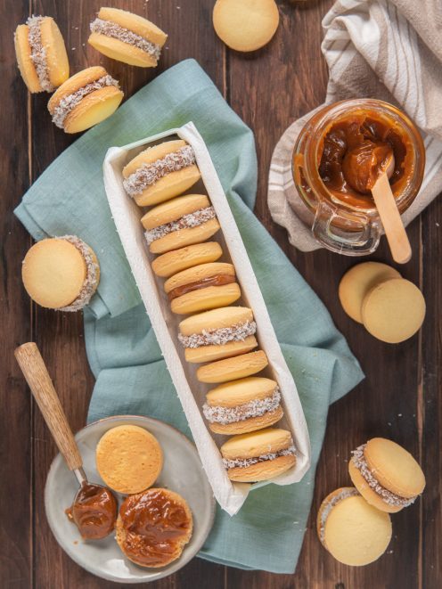 Alfajores farciti di dulce de leche e bordati di cocco disposti in fila accanto al vasetto di crema