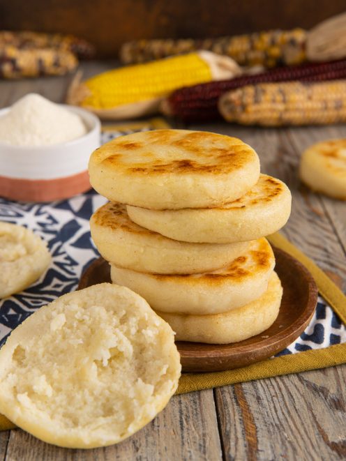 Arepas di mais impilate con superficie dorata e una spezzata che mostra l'interno morbido