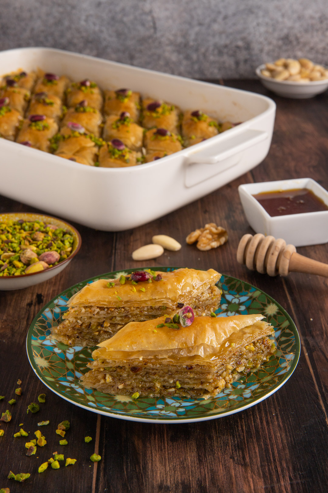 Porzioni di baklava a strati sfogliati con granella di pistacchi e petali di rosa, servite su piatto decorato