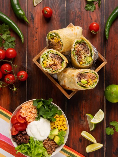 Burrito tagliato a metà con riso, mais, fagioli e avocado, servito con una bowl degli stessi ingredienti