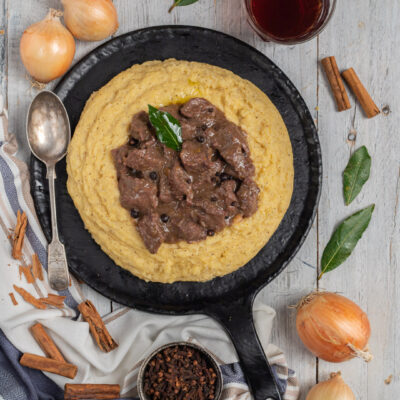 Carbonada con polenta cremosa servita in padella di ferro, guarnita con una foglia di alloro
