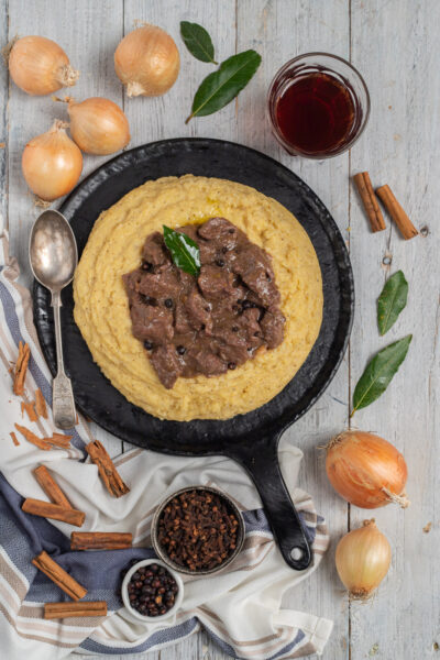 Carbonada con polenta cremosa servita in padella di ferro, guarnita con una foglia di alloro