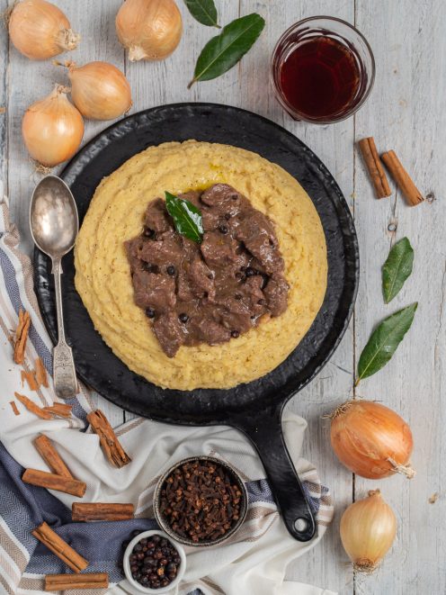 Carbonada con polenta cremosa servita in padella di ferro, guarnita con una foglia di alloro