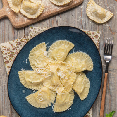 Cjalsons de Timau conditi e cosparsi di formaggio grattugiato, con altri fagottini crudi infarinati sul tagliere
