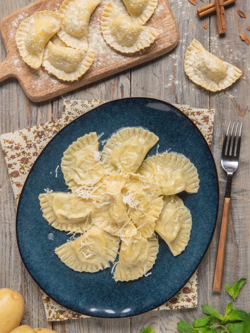 Cjalsons de Timau conditi e cosparsi di formaggio grattugiato, con altri fagottini crudi infarinati sul tagliere
