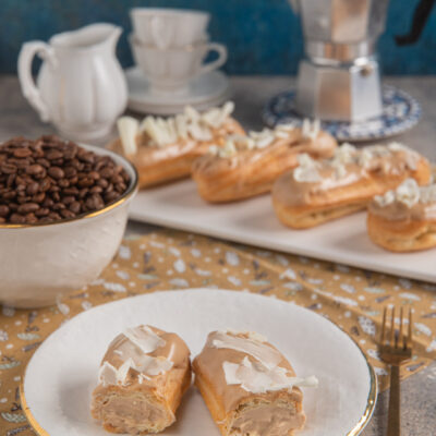 Eclairs al caffè tagliati a metà con glassa e scaglie di cioccolato bianco, farciti di crema al caffè