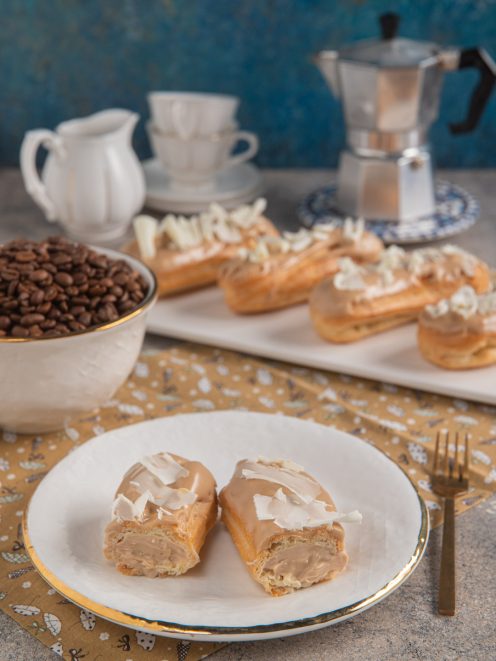 Eclairs al caffè tagliati a metà con glassa e scaglie di cioccolato bianco, farciti di crema al caffè