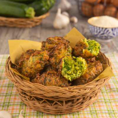 Frittelle di zucchine fritte e dorate, una spezzata a metà rivela il ripieno verde