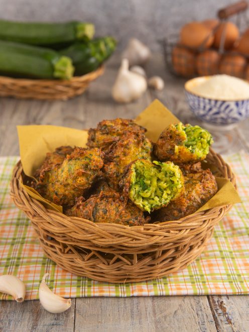 Frittelle di zucchine fritte e dorate, una spezzata a metà rivela il ripieno verde
