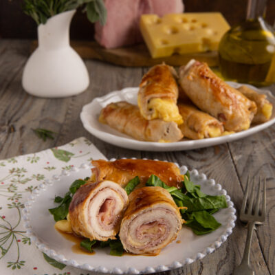 Involtini di pollo ripieni di prosciutto e formaggio, serviti su foglie di spinaci con fondo di cottura