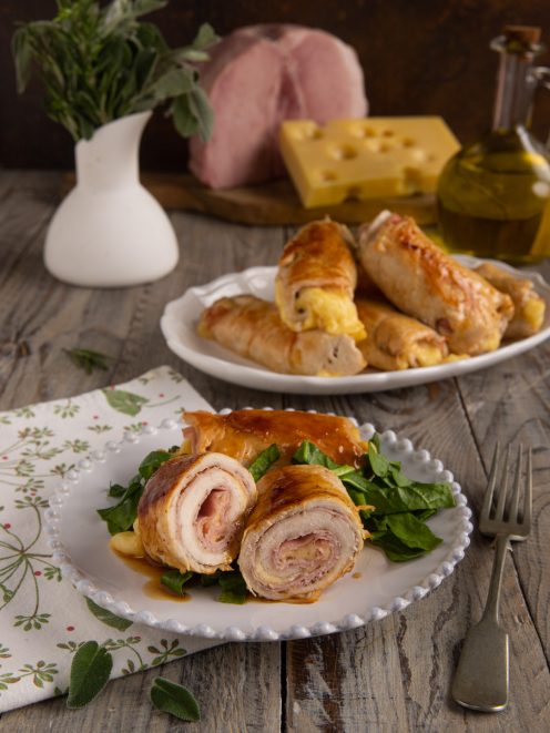 Involtini di pollo ripieni di prosciutto e formaggio, serviti su foglie di spinaci con fondo di cottura