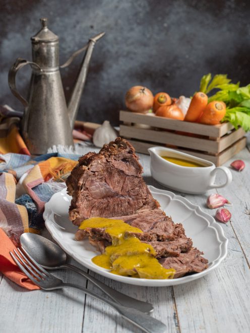 Manzo all'olio affettato e nappato con salsa gialla, servito su piatto da portata