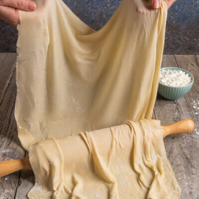 Pasta fillo sottile e trasparente sollevata a mano sopra un mattarello infarinato