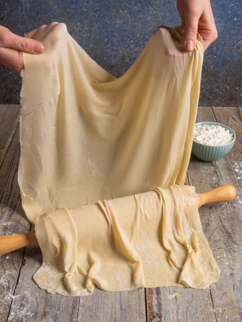 Pasta fillo sottile e trasparente sollevata a mano sopra un mattarello infarinato