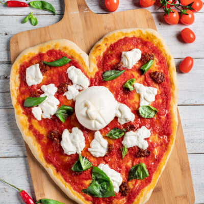 Pizza a forma di cuore con salsa di pomodoro, burrata intera al centro e foglie di basilico