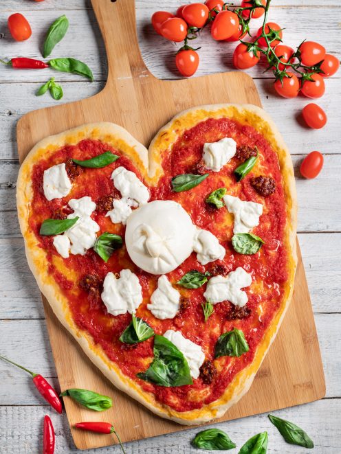 Pizza a forma di cuore con salsa di pomodoro, burrata intera al centro e foglie di basilico