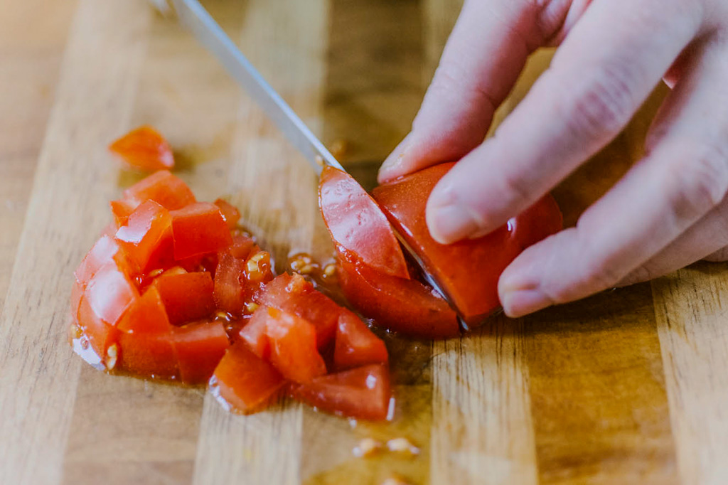 Mani che tagliano un pomodoro a cubetti su un tagliere di legno