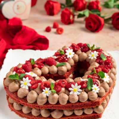 Red velvet cream tart a forma di cuore con ciuffi di crema al cioccolato, lamponi e fragole fresche