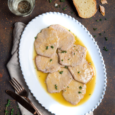 Scaloppine al vino bianco con salsa dorata e timo fresco, servite su vassoio ovale