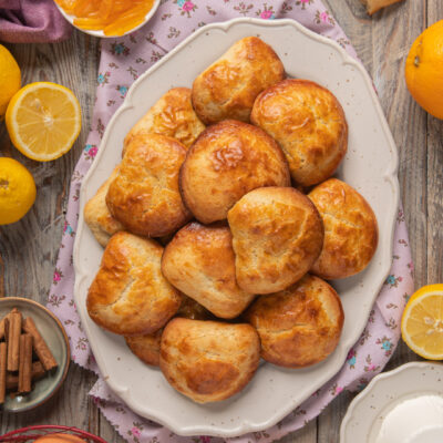 Sfogliatelle frolla dorate impilate su un piatto, circondate da agrumi e canditi all'arancia