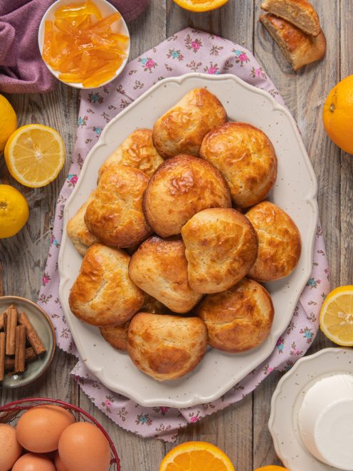 Sfogliatelle frolla dorate impilate su un piatto, circondate da agrumi e canditi all'arancia