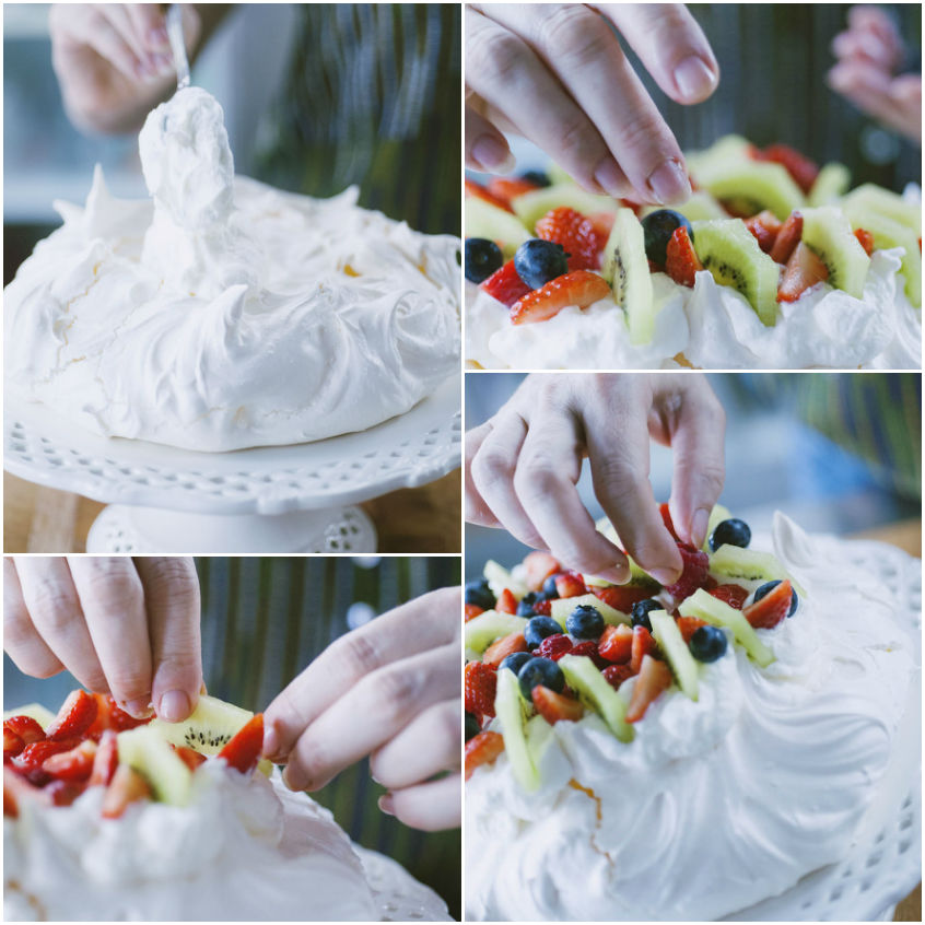 Mani che dispongono fragole, kiwi e mirtilli sulla pavlova già montata a meringa