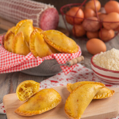 Calascione laziale dorato con la pasta sfogliata in primo piano, uno spezzato rivela il ripieno