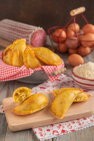 Calascione laziale dorato con la pasta sfogliata in primo piano, uno spezzato rivela il ripieno