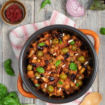 Caponata siciliana in tegame con melanzane, olive verdi, pinoli e foglie di basilico fresco