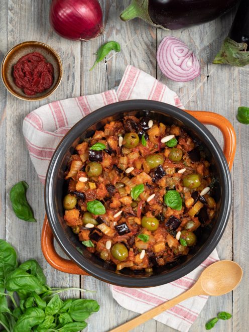 Caponata siciliana in tegame con melanzane, olive verdi, pinoli e foglie di basilico fresco