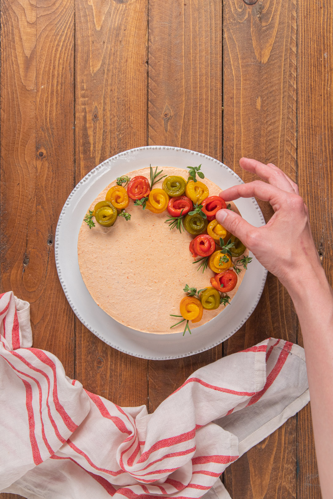 Mano posiziona roselline di peperoni arrostiti sulla superficie della cheesecake salata con rametti di erbe aromatiche