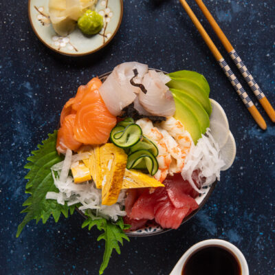 Chirashi con salmone, tonno, gamberi e avocado su daikon e foglie di shiso