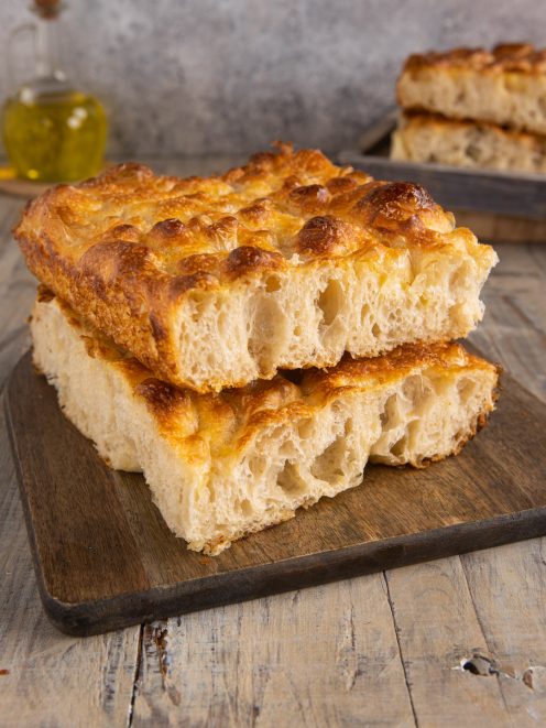 Focaccia bollosa tagliata a fette impilate che mostrano l'alveolatura soffice e la crosta dorata