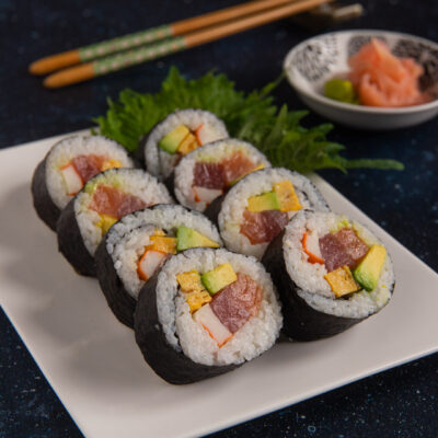 Futomaki tagliati a fette con tonno, avocado, surimi e frittata, serviti su foglie di shiso