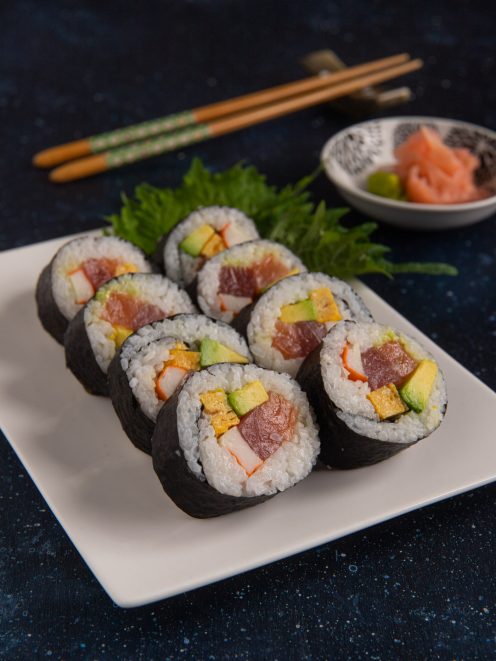 Futomaki tagliati a fette con tonno, avocado, surimi e frittata, serviti su foglie di shiso