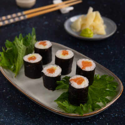 Hosomaki al salmone avvolti in alga nori, serviti su foglie di shiso