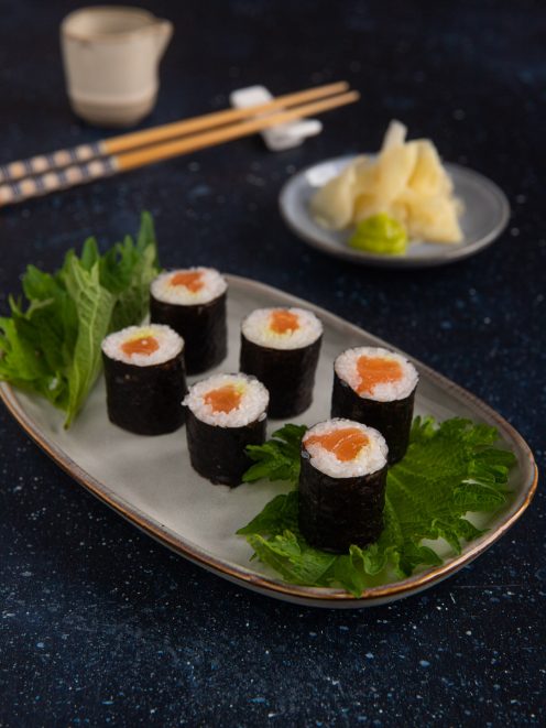 Hosomaki al salmone avvolti in alga nori, serviti su foglie di shiso