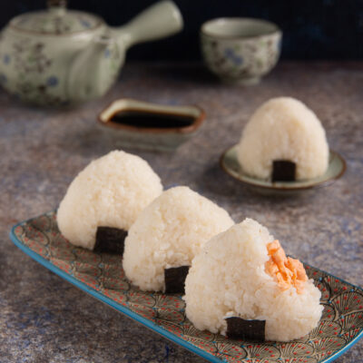 Gli onigiri sono una tipologia di sushi costituita da polpette di riso a forma triangolare con un ripieno di salmone e parzialmente avvolte da una striscia di alga Nori che le rende facili da mangiare con le mani
