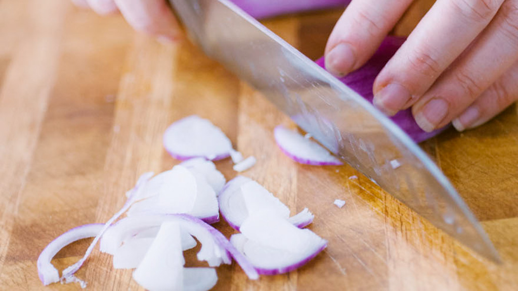 Cipolla rossa affettata a mezzalune sul tagliere con coltello da chef