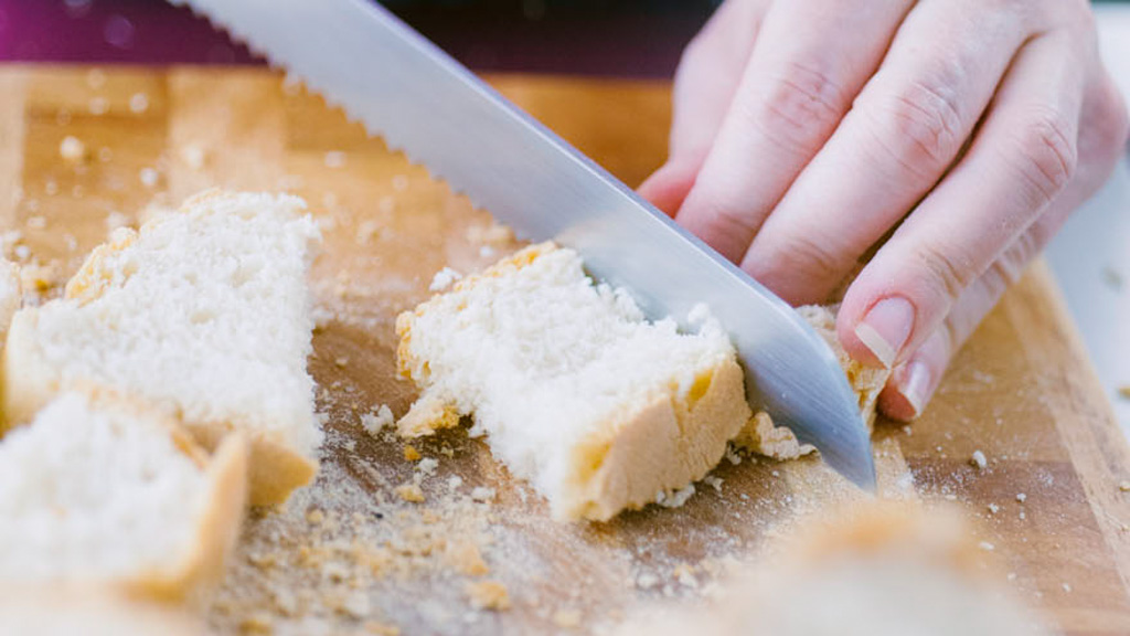 Mano che taglia il pane raffermo a pezzetti irregolari sul tagliere