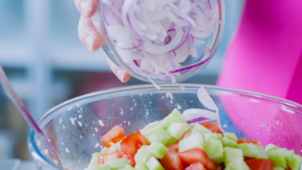 Cipolla rossa affettata versata su pomodori e cetrioli a cubetti per la panzanella