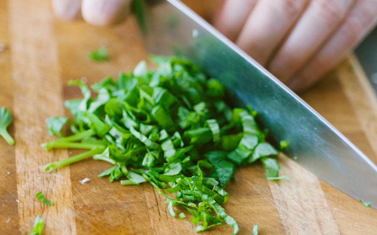 Basilico tritato finemente sul tagliere con un coltello da chef