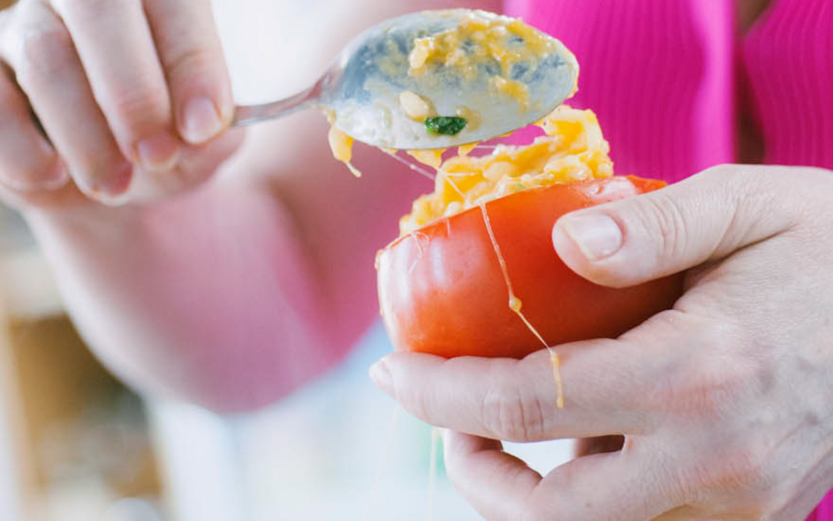 Mani che farciscono un pomodoro svuotato con il risotto usando un cucchiaio