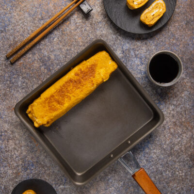 Tamagoyaki appena arrotolato nella padella rettangolare, con fette già tagliate che mostrano gli strati interni
